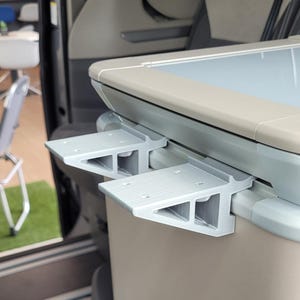 Könnte beinhalten: Ein hellgraues, 3D-gedrucktes Regalsystem für Fahrzeuginnenräume. Das System umfasst zwei rechteckige Regale mit einer Stützstruktur, die an einer beigefarbenen Platte befestigt sind. Die Regale sind etwa 15 cm lang.