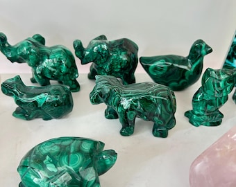 May include: A collection of small animal figurines carved from green malachite stone, including an elephant, a turtle, a bird, and other creatures. Each piece displays the characteristic dark and light green banded patterns of the mineral.