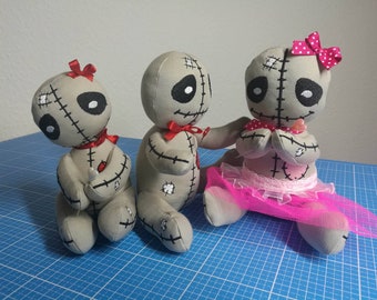 May include: Three handmade rag dolls with stitched details. The dolls are gray with black eyes and red bows. One doll is wearing a pink tulle skirt.