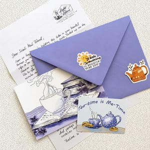以下が含まれることがあります： A little something to brighten your dayと書かれた太陽のステッカーとティーポットのステッカーが貼られたラベンダー色の封筒。手書きの手紙、本の上に湯気の立つカップが描かれたポストカード、Tea-time is Me-Timeと書かれたカードが入っています。