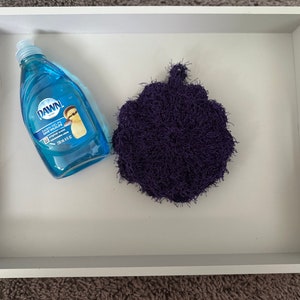 Puede incluir: Una bandeja blanca con una botella de jabón lavavajillas azul etiquetada como "DAWN" y una esponja de fregar morada.