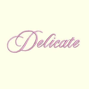 May include: The word "Delicate" embroidered in a cursive script with a light pink thread. The text is centered on a cream-colored background, showcasing the elegant design.