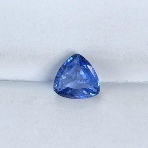 May include: A triangular blue sapphire gemstone with a faceted cut.
