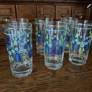 May include: Set of six clear glass drinking glasses with a blue and green floral pattern. The glasses have a light blue rim.