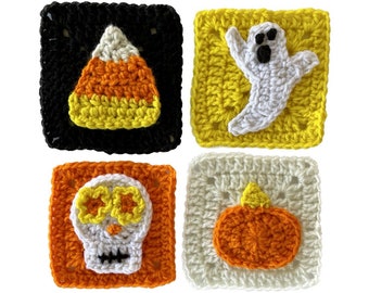 Op de afbeelding: Vier gehaakte vierkanten met Halloween-thema's. De vierkanten tonen een snoepmais, een spook, een schedel en een pompoen. De vierkanten zijn gemaakt van oranje, geel, wit en zwart garen.