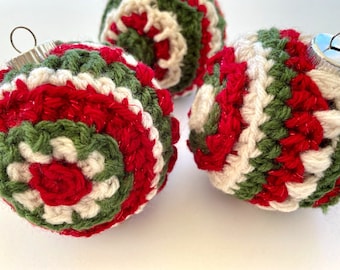 May include: Three crocheted Christmas ornaments in red, green, and white. The ornaments are made with a spiral pattern and have a shiny finish.