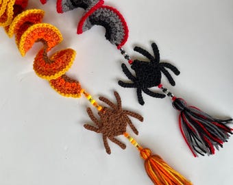 May include: Two crocheted spider ornaments with black and brown bodies and red and yellow beaded tails. The spiders are hanging from crocheted orange and gray swirls.