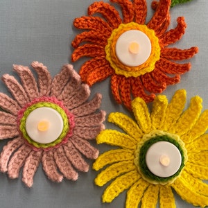 May include: Three crocheted flower candle holders in pink, orange, and yellow. Each flower has a small tea light candle in the center.