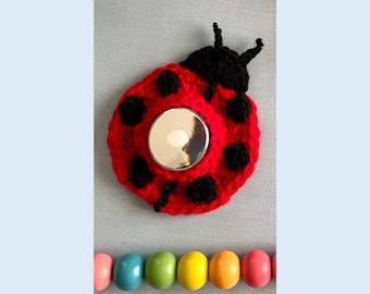May include: A red crocheted ladybug tea light holder with black spots and a silver metal tea light insert.