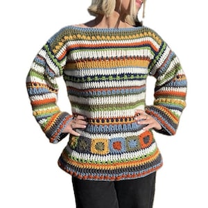 May include: A colorful striped crochet sweater with a geometric pattern at the bottom. The sweater has long sleeves and a wide neckline.