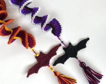 Puede incluir: Tres adornos de murciélago de ganchillo con colas de hilo de colores. Los murciélagos son morados, negros y granate. Las colas están hechas de hilo en tonos naranja, amarillo y blanco.