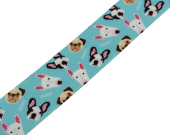 May include: A light blue ribbon with a repeating pattern of dog faces, including pugs, French bulldogs, and white terriers. The word "DOGS" is printed in white between the dog faces. The ribbon is angled diagonally.