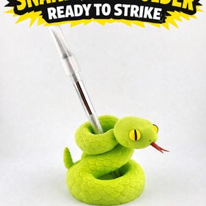 May include: A lime green snake-shaped tool holder with a red tongue and yellow eyes, holding a silver and clear tool. The text "SNAKE TOOL HOLDER READY TO STRIKE" is above the snake.