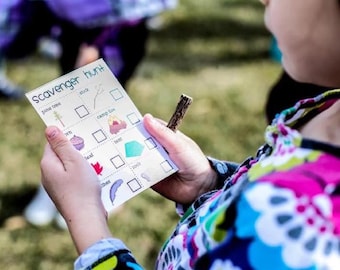 May include: A white card with the words "Scavenger Hunt" printed on it. The card has a list of items to find, including a pine tree, a stick, a camp fire, a tent, a leaf, and a feather. The card is being held by a child.