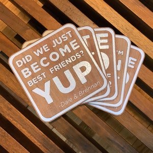May include: A set of six wooden coasters with a white background and silver lettering. The coasters feature the text "Did we just become best friends? Yup - Dale & Brennan".