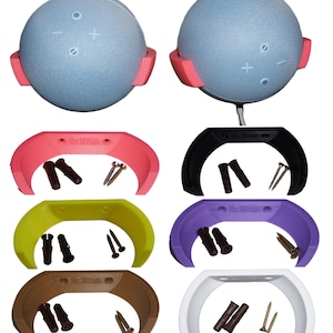 Könnte beinhalten: Ein hellblauer Smart-Lautsprecher mit rosa Halterung und mehrere farbige Wandhalterungen. Die Wandhalterungen sind in Pink, Schwarz, Gelb, Lila, Braun und Weiß erhältlich. Jede Halterung enthält Schrauben und Wandanker. Der Lautsprecher hat Lautstärke- und Aktionstasten.