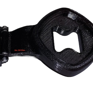 Può includere: Apribottiglie nero stampato in 3D con una forma unica. L'apribottiglie presenta un'apertura quadrata e una base a cerniera. Il testo "Alec 3D Prints" è visibile. Progettato per un facile utilizzo.