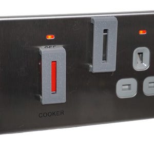 Può includere: Una presa elettrica grigio scuro con un interruttore per fornelli e due prese aggiuntive. L'interruttore per fornelli ha una spia rossa e la scritta "COOKER" stampata sotto. Sono attaccate due coperture di plastica grigia.