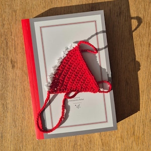 May include: A red and white crocheted triangle with a white border. The triangle is on top of a book with the text "Beyond" and "Aleksandra Rekar" on the cover.