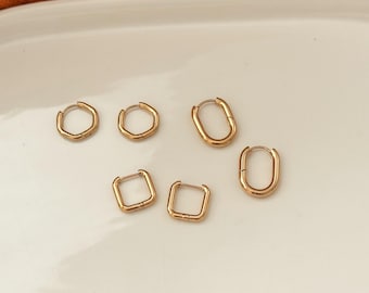 May include: Gold-colored hoop earrings in various shapes: round, oval, and square. The earrings are displayed on a white surface, with an orange background. The earrings are small and appear to be made of metal.
