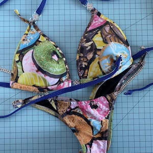 Puede incluir: Un bikini azul y negro con estampado de donuts. La parte superior del bikini tiene un estilo halter y la parte inferior es un corte atrevido.
