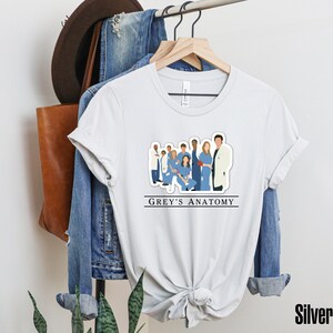 May include: White t-shirt with a graphic of the main characters from the TV show Grey's Anatomy. The text "GREY'S ANATOMY" is printed below the graphic.