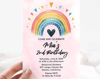 May include: A pink invitation with a rainbow and a heart. The text reads "Come and Celebrate Mia's 2nd Birthday. Saturday, June 8, 2024 at 4:30 in the afternoon. Botanical Gardens 327 Latigo Canyon Rd, Malibu, California. Please RSVP to Kelly By 11.12.23"