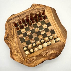 Puede incluir: Un juego de ajedrez de madera con un borde de borde vivo. El tablero presenta cuadrados oscuros y claros alternos, con piezas de ajedrez en su lugar. Las piezas son marrones y blancas. El tablero es de madera de olivo.