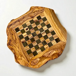 Puede incluir: Un tablero de ajedrez de madera hecho a mano con borde natural. La superficie de juego presenta un patr&oacute;n de tablero de ajedrez de cuadrados claros y oscuros. El tablero est&aacute; hecho de madera de olivo, mostrando la veta.