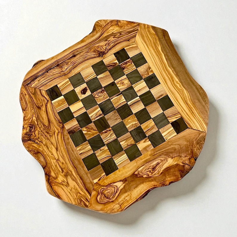 Puede incluir: Un tablero de ajedrez de madera hecho a mano con borde natural. La superficie de juego presenta un patr&oacute;n de tablero de ajedrez de cuadrados claros y oscuros. El tablero est&aacute; hecho de madera de olivo, mostrando la veta.