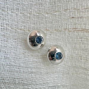 May include: A pair of silver stud earrings with a small blue gemstone in the center of each earring.