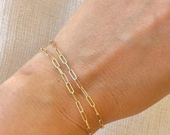 May include: A delicate gold bracelet featuring a series of elongated, rectangular paperclip-style links. The chain is composed of polished, metallic gold-toned segments connected in a continuous, repeating pattern that wraps around the wrist.
