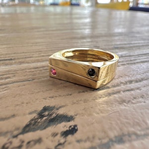 May include: A gold ring with a square design and three black and pink gemstones.