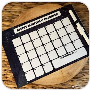 May include: A black and white dry erase monthly planner with a space theme. The planner has a white border and white squares for each day of the month. The text "Alfies Monthly Planner" is at the top of the planner. The text "The Month Is..." is at the bottom of the planner.