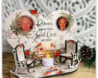 May include: A heart-shaped wooden memorial with two framed photos, the text "Robins appear when Loved Ones are near", and two miniature rocking chairs. The design includes floral and bird accents, and a small LED candle.
