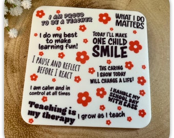 May include: White coaster with red flower designs and black text. The text reads: "I am proud to be a teacher", "I do my best to make learning fun!", "I pause and reflect before I react", "I am calm and in control at all times", "Teaching is my therapy I grow as I teach", "What I do matters", "Today I'll make one child smile", "The caring I show today will change a life!", "I handle my school day with ease".