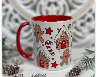 May include: White ceramic mug with a red interior and handle. The mug is decorated with gingerbread men, gingerbread houses, red stars, and candy canes. A festive holiday-themed mug.
