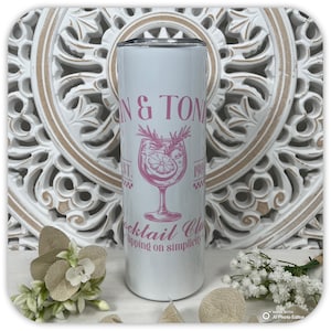 May include: A white tumbler with a pink design that reads "GIN & TONIC Cocktail Club" with a cocktail glass illustration. The tumbler also has the text "EST. 198" and "Sipping on simplicity."