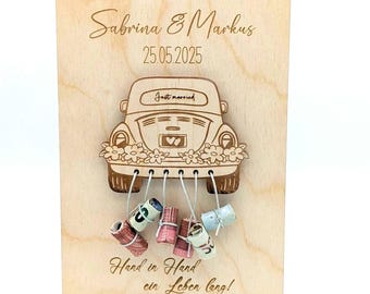 Könnte beinhalten: Holzhochzeitsschild mit einem Auto-Design, floralen Details und den Worten "Just Married". Die Namen "Sabrina & Markus" und das Datum "25.05.2025" sind eingraviert. Der Satz "Hand in Hand ein Leben lang!" steht unten.