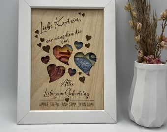 May include: A white framed wooden sign with a laser-cut design of hearts. The hearts are filled with money. The sign reads "Liebe Kerstin, wir wünschen dir von Alles Liebe zum Geburtstag NADINE, STEFAN, ENNA STINA, LUCIAN, NOAH".