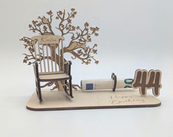 May include: Wooden birthday card with a rocking chair, a tree, and a money holder. The card says "Happy Birthday" and has the number "44" on it. The rocking chair has the name "Kristin" on the back.
