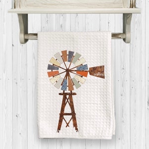 May include: A white kitchen towel with a brown windmill design. The windmill has a rusty brown base and a multi-colored wheel with a variety of patterns. The text "restless" is printed on the towel.