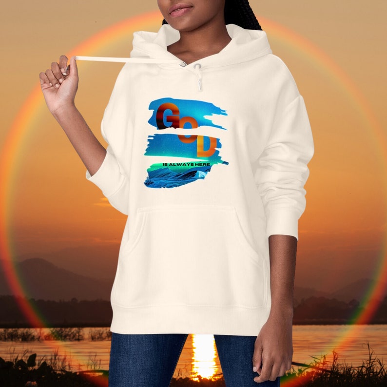May include: Off-white hoodie with a front graphic. The graphic displays the word "GOD" in orange and black, with the text "IS ALWAYS HERE" underneath. The background shows a rainbow and a sunset.