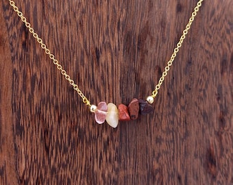 May include: A gold chain necklace with a row of small, colorful stones. The stones are pink, orange, yellow, red, and brown.