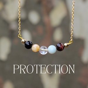 May include: A gold chain necklace with a row of colorful gemstone beads. The beads include black, yellow, clear, light blue, and red-brown stones. The word "PROTECTION" is displayed in white text below the necklace.