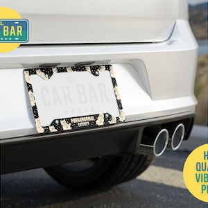 Puede incluir: Marco de matr&iacute;cula negro y blanco con un dise&ntilde;o de gato. El marco tiene el texto "The Car Bar" y "Purranormal Cativity".