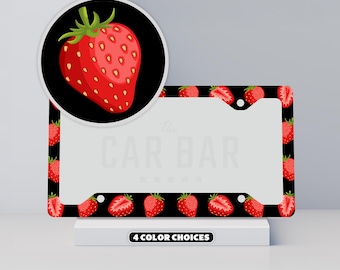 May include: A rectangular black license plate frame featuring a repeating pattern of red strawberries and strawberry slices. A circular inset shows a detailed view of a single red strawberry on a black background. The text 4 COLOR CHOICES appears.