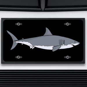 May include: A black and white illustration of a great white shark on a black background. The shark is facing right and has a white underbelly. The image is framed with a black border.