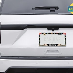 May include: A black license plate frame with a floral design and the text "The Car Bar" and "Read Between The Books".