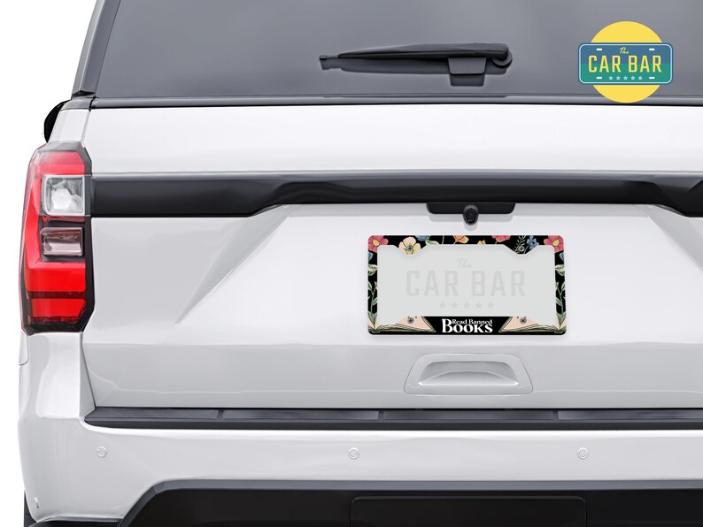 May include: A black license plate frame with a floral design and the text "The Car Bar" and "Read Between The Books".
